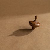 Wooden spinning top with a long shadow on brown paper